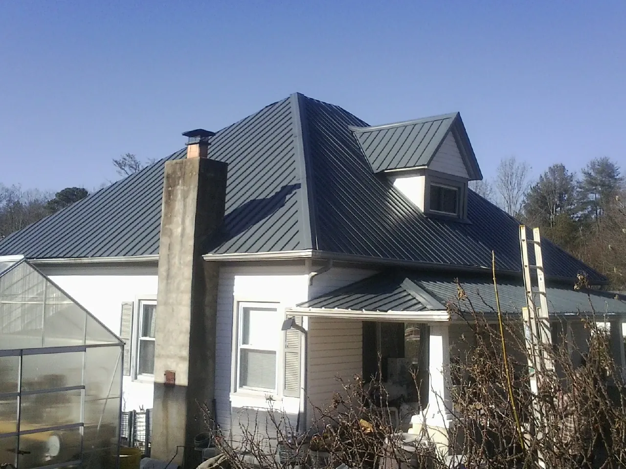 Dark blue standing seam metal roof on a white farmhouse with dormer — Slate & Tile Roof Repair by Roofing Brothers in Milford Square