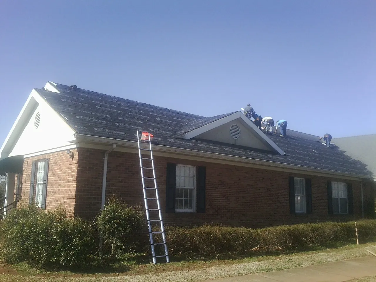 Crew tearing shingles off a brick ranch roof with a ladder set — Metal Roof Repair work by our crew in Milford Square