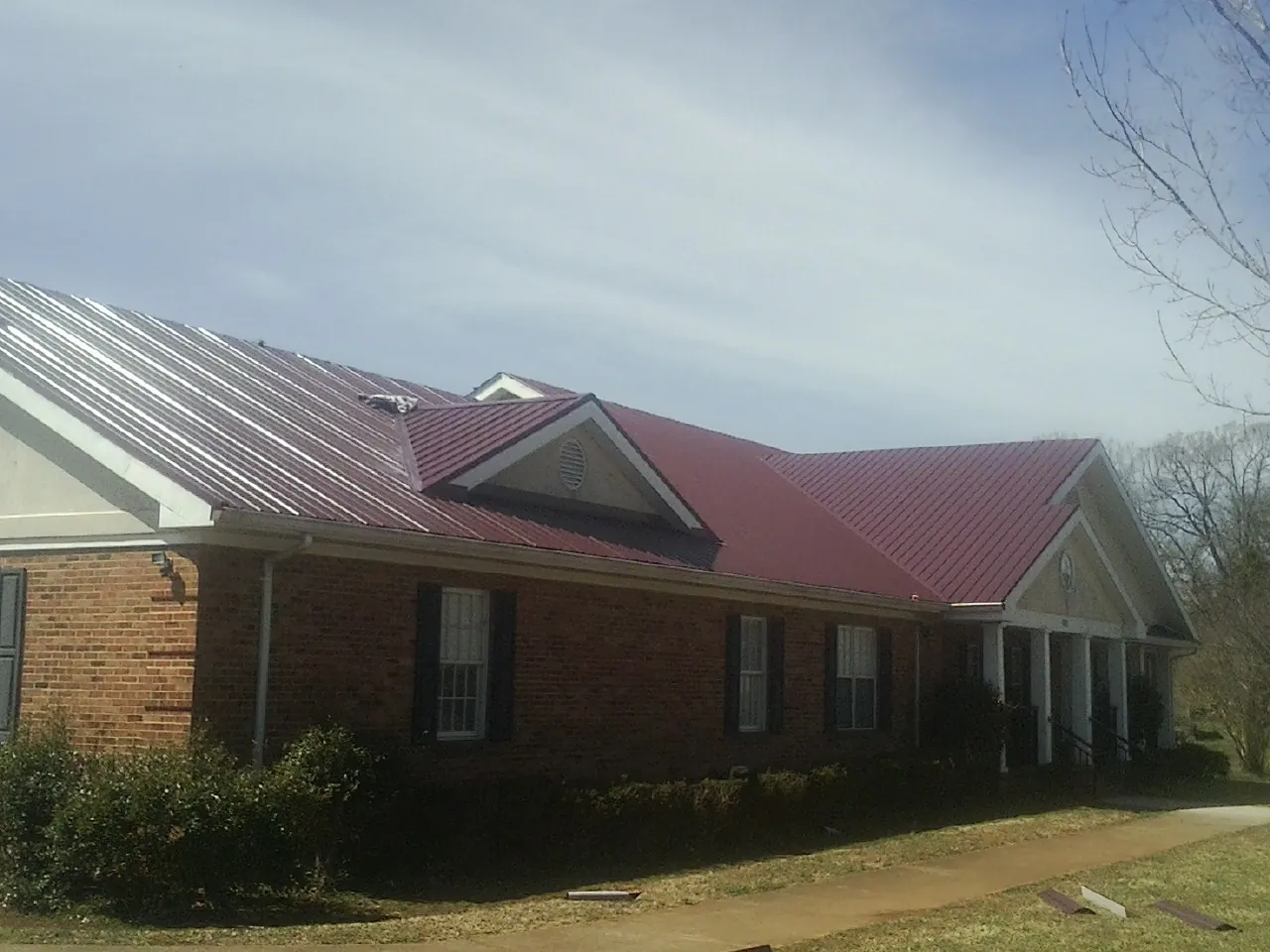 Red metal roof with gabled entries on a long brick building, from a Hail Damage Roof Repair job in Milford Square