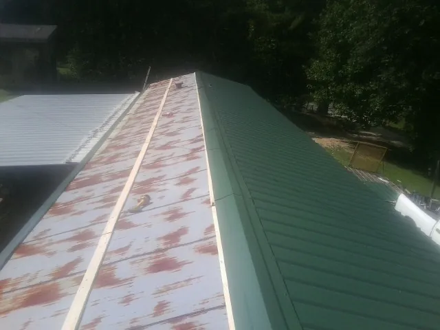 Old rusted panels beside newly installed green metal roofing — Wind Damage Roof Repair by Roofing Brothers in Milford Square