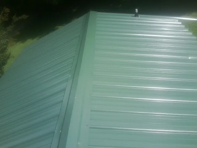 New green metal panels meeting at the ridge of a roof — Flat Roof Repair work by our crew in Milford Square
