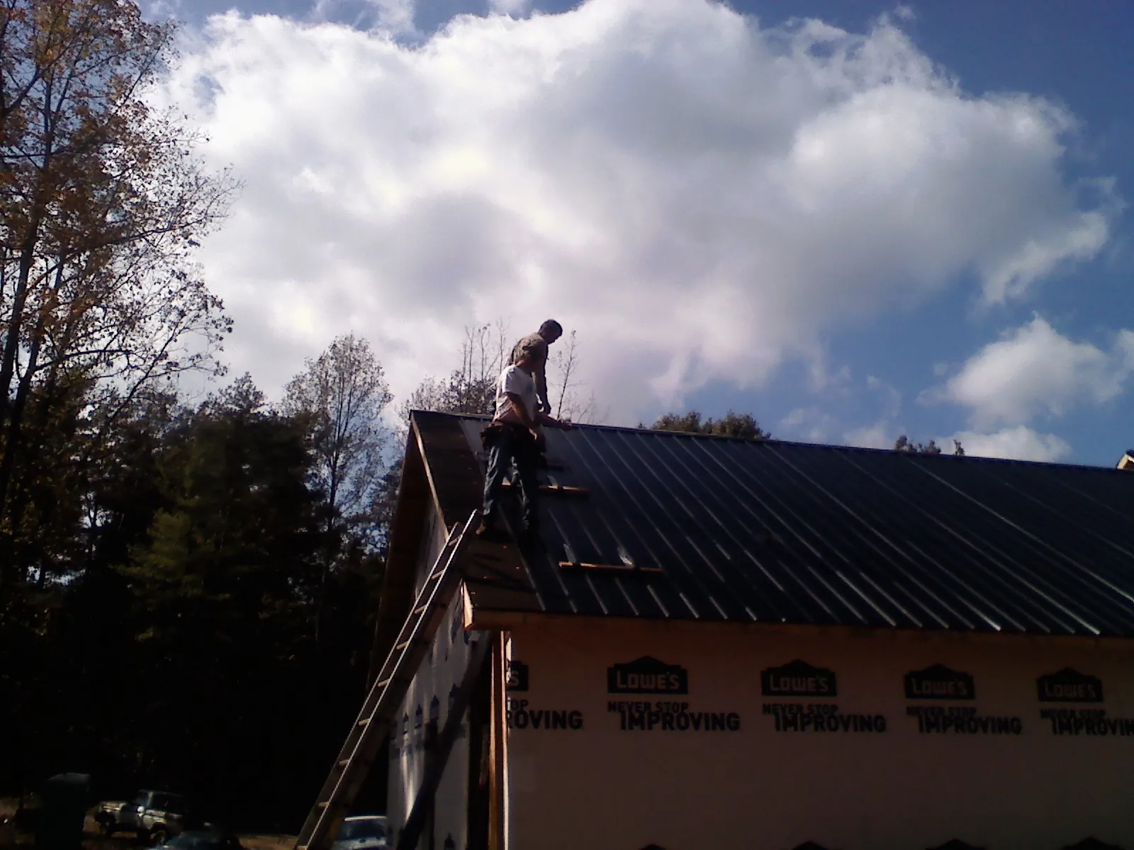 Roofer fastening dark metal panels high against a cloudy sky, from a Roof Inspection job in Milford Square