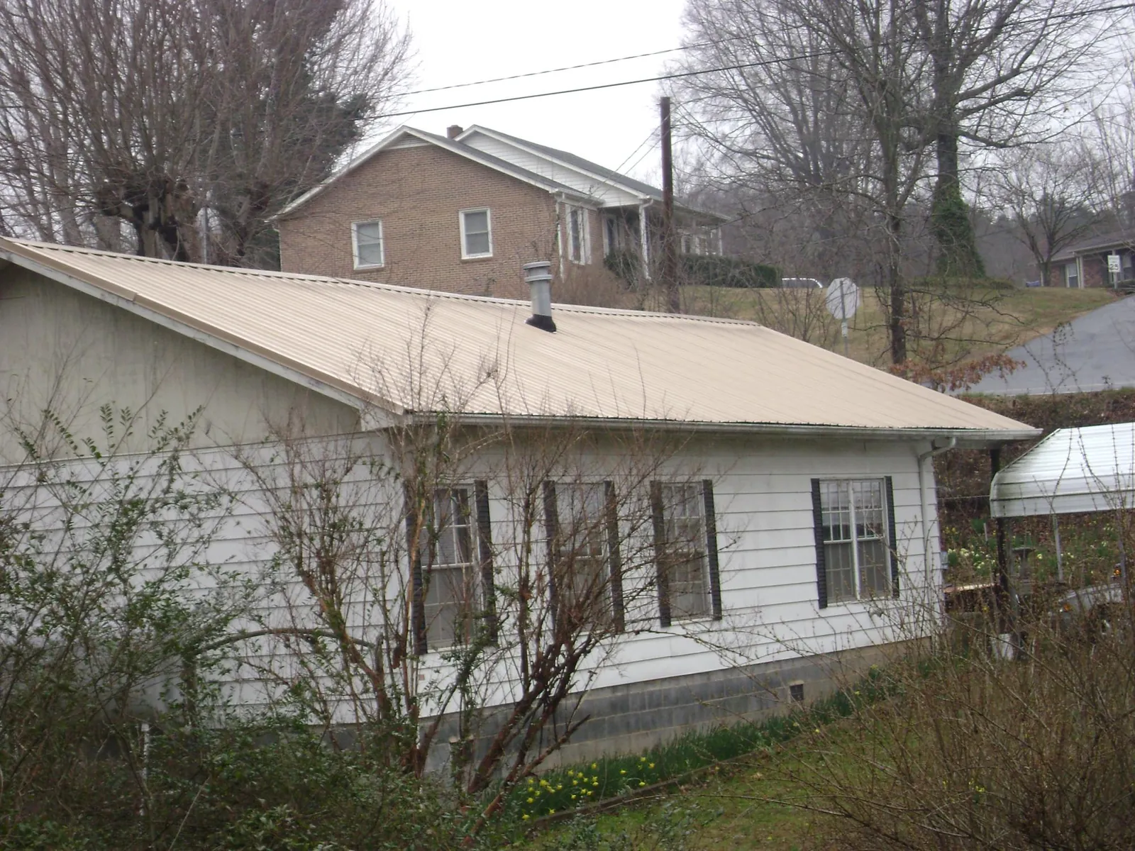 Tan metal roof on a white sided house set into a hillside — Commercial Roofing by Roofing Brothers in Milford Square