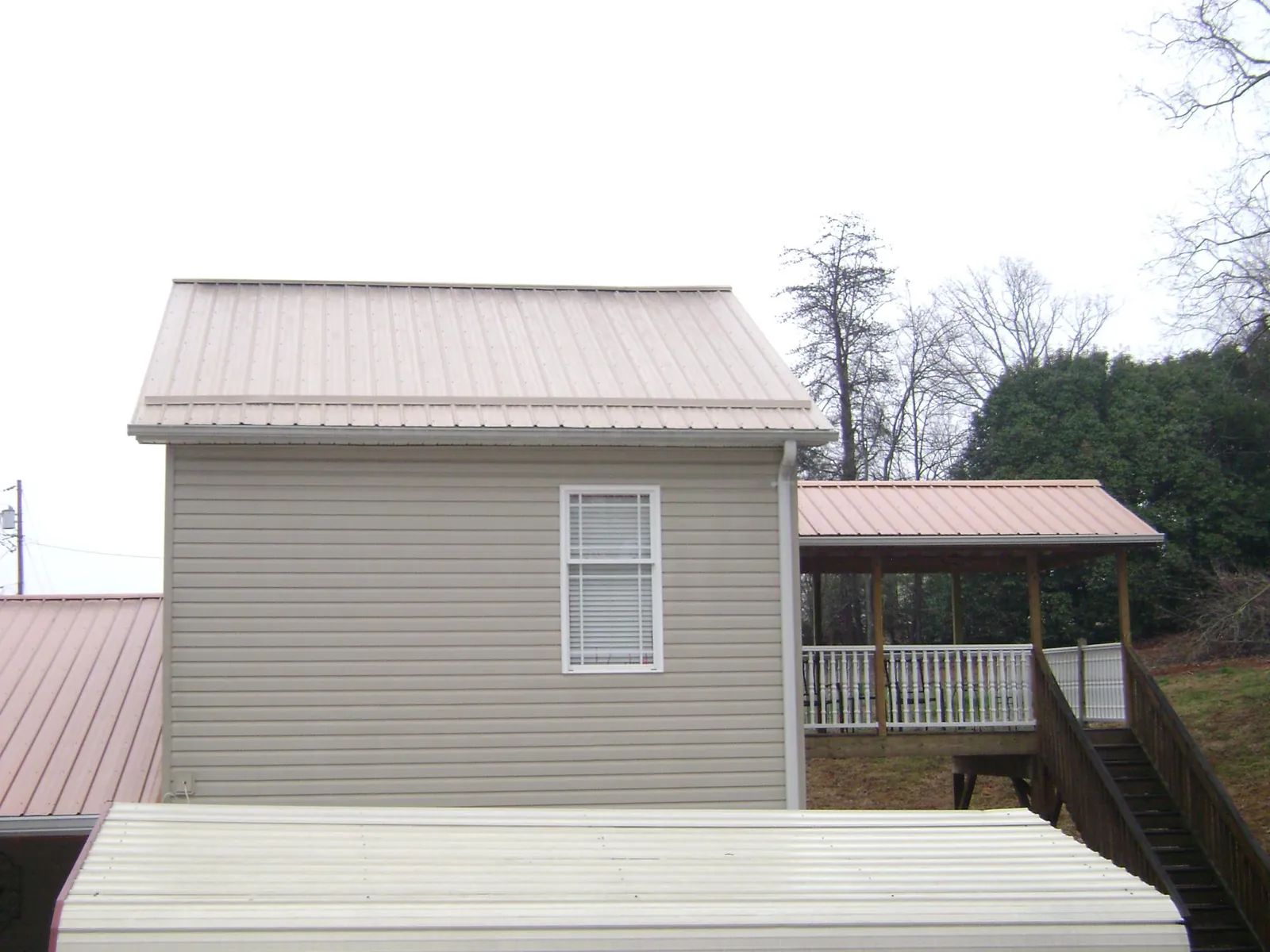 Tan metal roofs on a two story addition and attached porch, from a Roof Replacement job in Milford Square